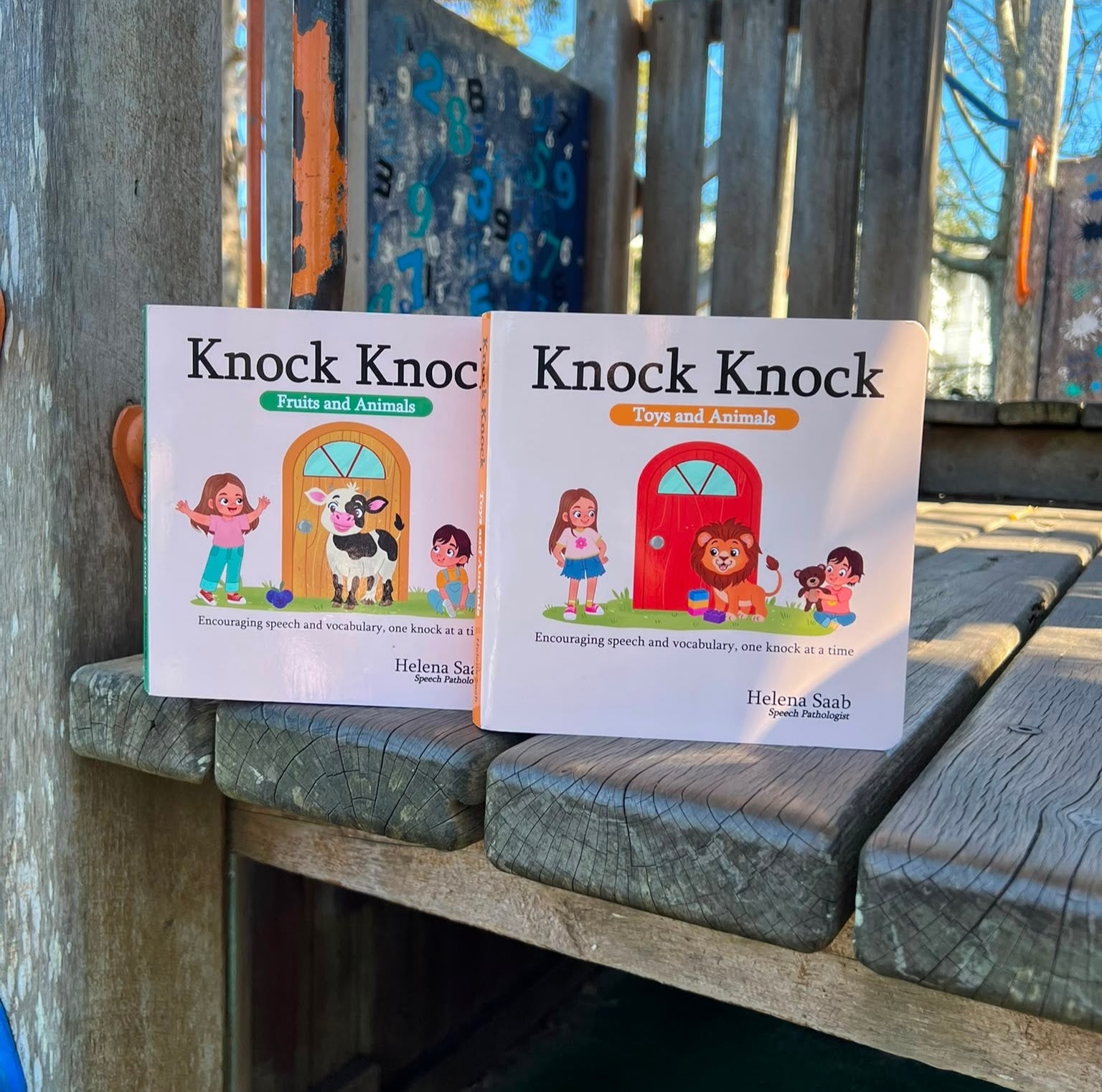 The Speechie Mumma Knock Knock board books, Fruits and Animals and Toys and Animals, displayed outdoors on a playground, encouraging speech and vocabulary development for toddlers